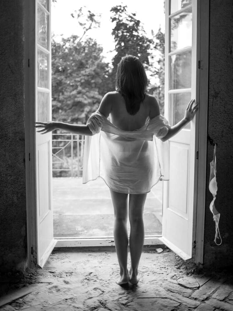 Eine junge Frau steht leicht bekleidet an einer offenen Tür. Das Foto ist in Schwarz-Weiß. Fotograf: Harald Baumeister aus Freinsheim.