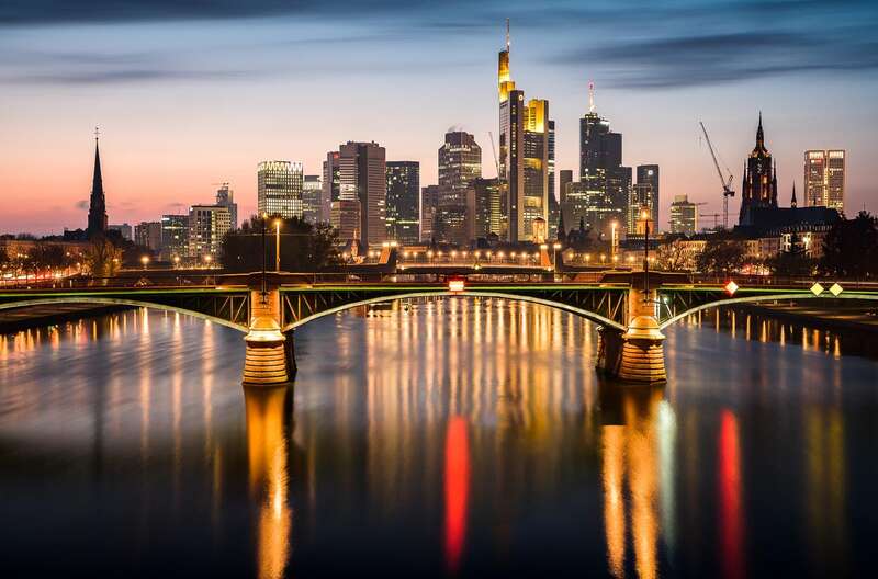 Die Frankfurter Skyline in der Blauen Stunde mit dem Main im Vordergrund, im Main spiegeln sich die Lichter der Stadt, ein Foto von Heimatlicht Florian Orth, entstanden bei einem Workshop in Frankfurt am Main